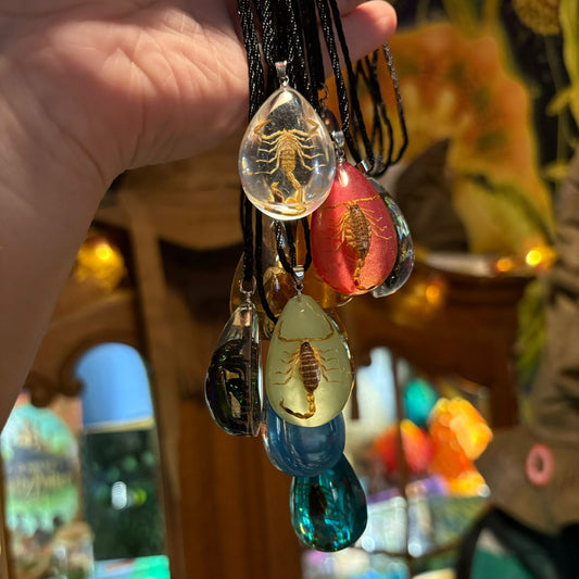 Hand holding a necklace with scorpion and beetle-themed glass pendants against a blurred background